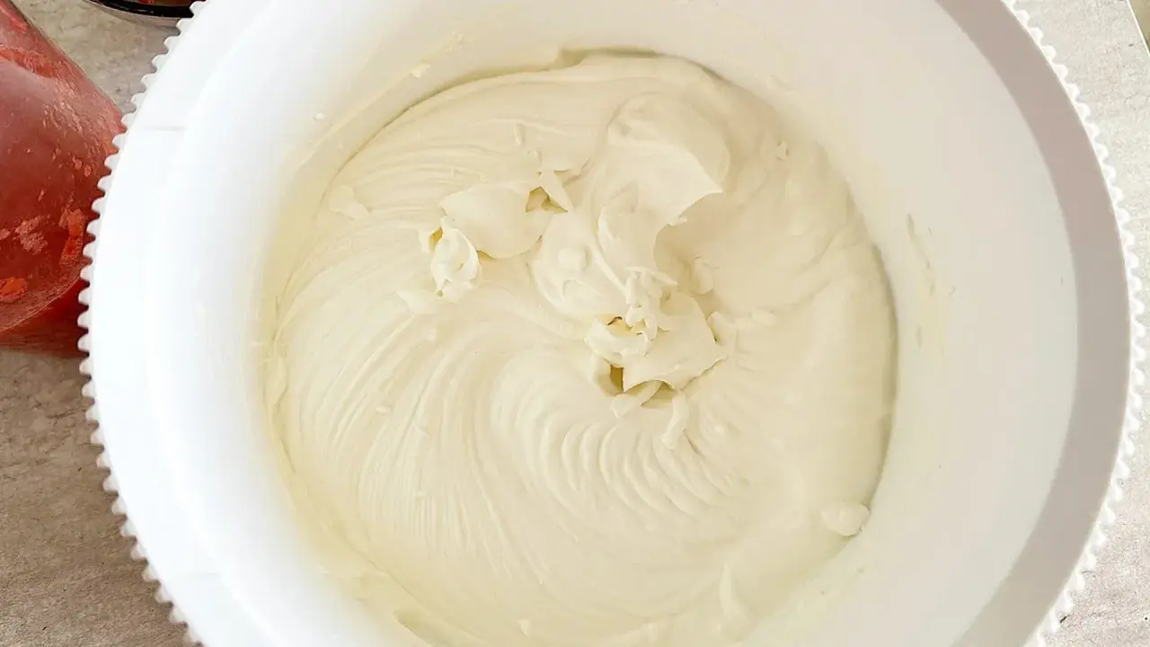 Gładki, puszysty krem z mascarpone w białej misie, gotowy do deseru. Obok miski widać miseczkę z truskawkami.