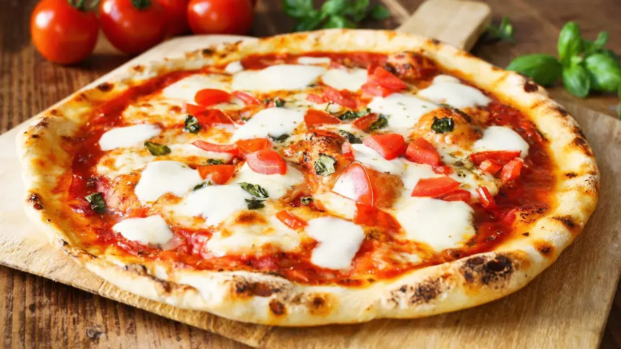 Pyszne ciasto na pizzę bez wyrastania, z pomidorami i mozzarellą, na drewnianej desce.