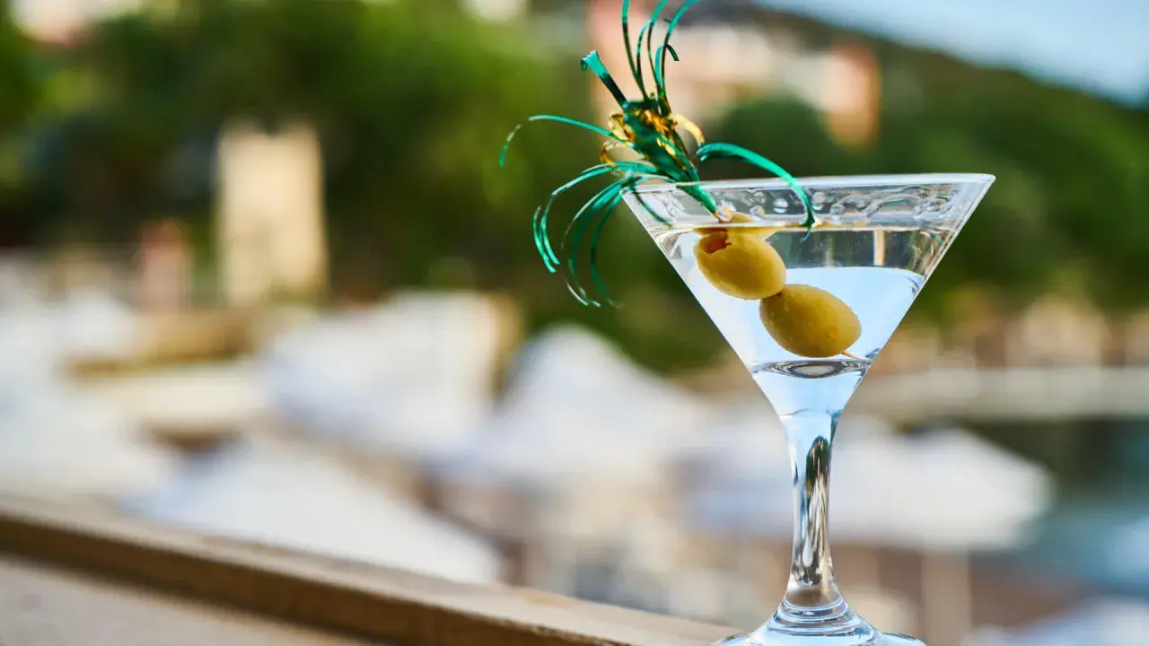 Orzeźwiający martini fiero drink z oliwkami, ozdobiony zieloną wstążką, na tle rozmytego, letniego krajobrazu.