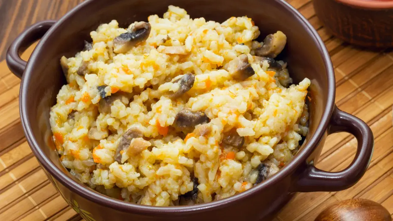 Pyszne risotto z warzywami, pełne grzybów i marchewki, podane w brązowej miseczce.