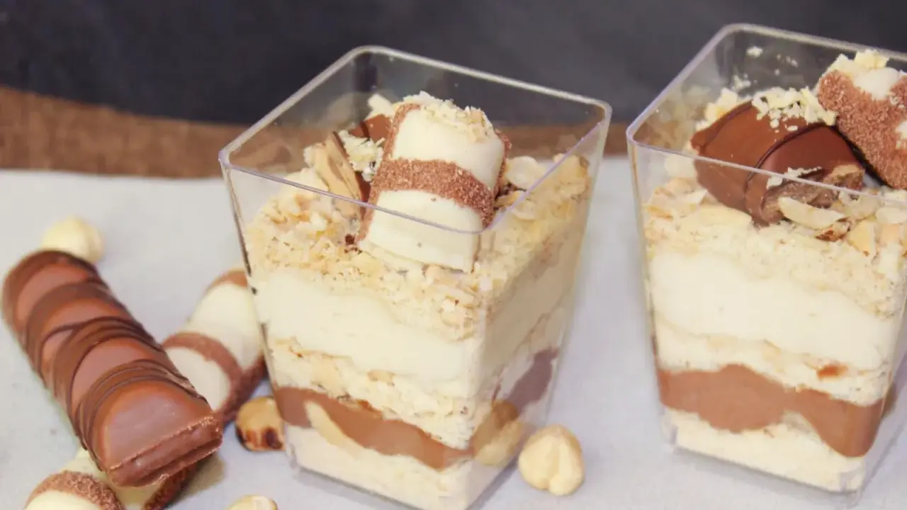 Pyszne ciasto Kinder Bueno w pucharkach, przełożone kremem i czekoladą, posypane orzechami.
