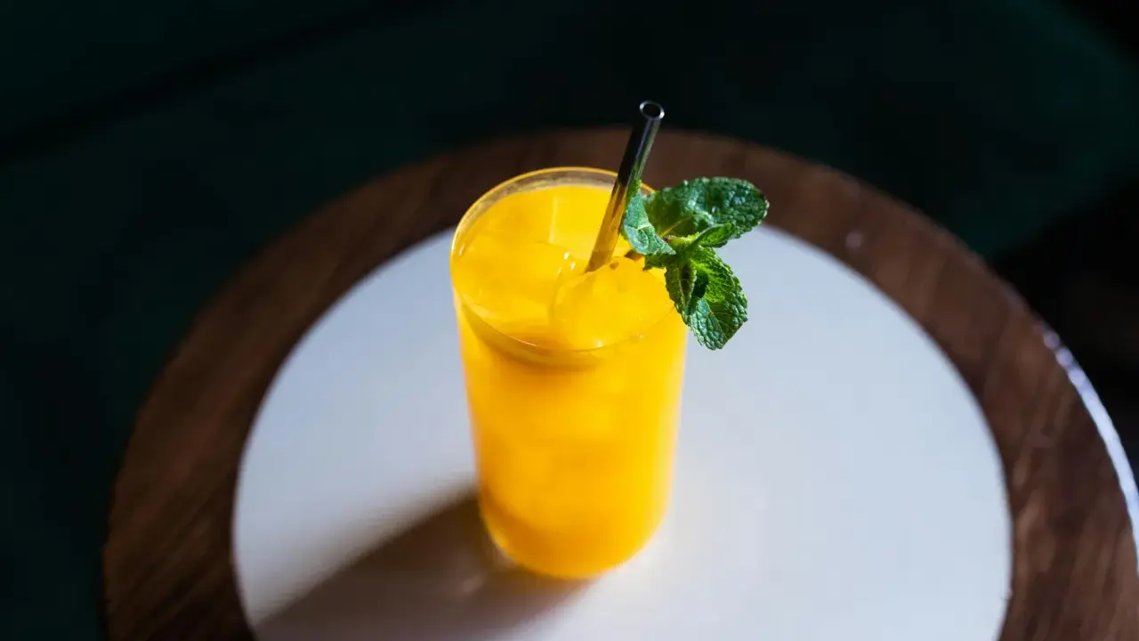 Orzeźwiający drink z mango, z kostkami lodu i listkiem mięty, podany w szklance ze słomką.