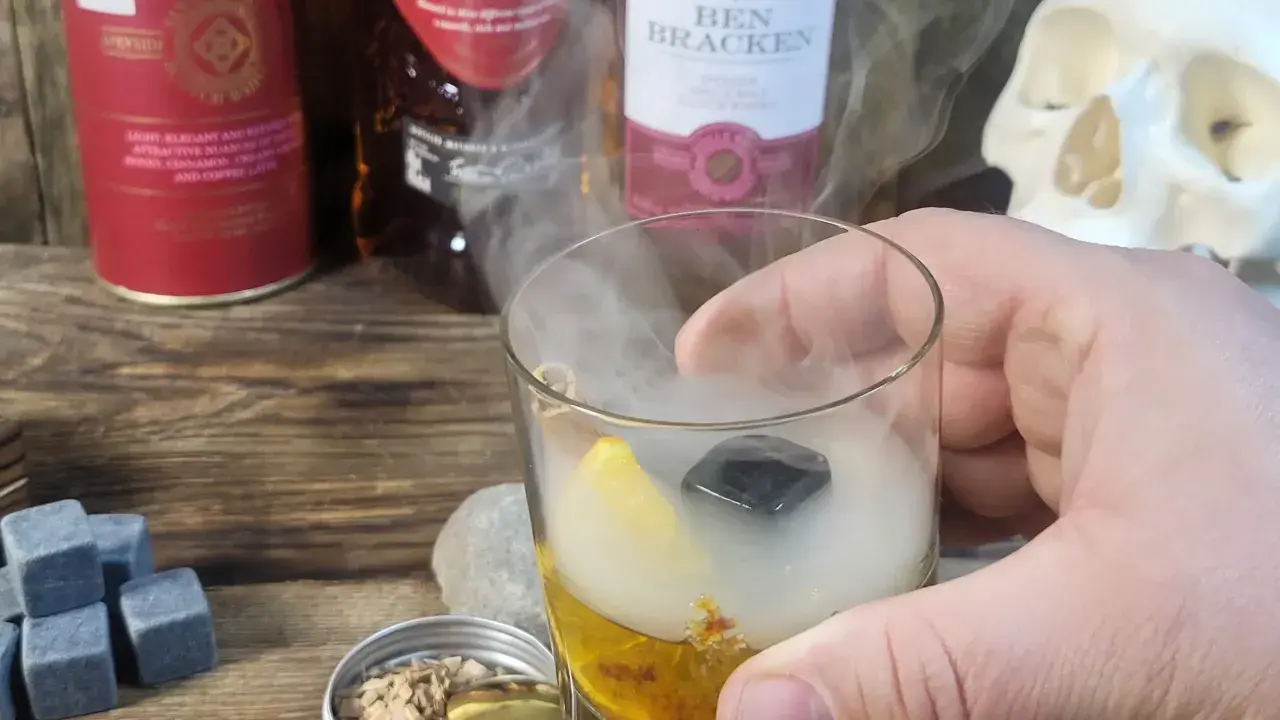 Szklanka z drinkiem otoczona dymem, obok butelki whisky i czaszka. Wyjątkowe drinki z dymem.