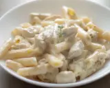 Penne z kurczakiem w kremowym sosie, udekorowane gałązką ziół. Pyszne danie, które zachwyci każdego smakosza.