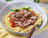 Pyszne spaghetti z bogatym sosem mięsnym na bazie passaty, posypane parmezanem i udekorowane listkami bazylii.