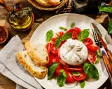 Pyszna burrata z pomidorami i bazylią, podana z chrupiącym pieczywem. To jest właśnie burrata – ser, który rozpływa się w ustach!