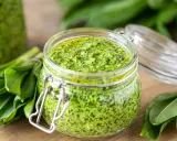 Słoik pełen aromatycznego pesto z czosnku niedźwiedziego, otoczony świeżymi liśćmi tej wiosennej rośliny.