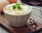 Aksamitny majonez domowy w miseczce, obok jajka, pieprz i trzepaczka. Idealny do sałatek!