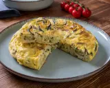 Pyszna frittata z cukinią, podana na talerzu, z pomidorkami koktajlowymi w tle.