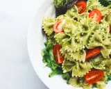 Makaron farfalle z zielonym pesto ze słoika, udekorowany połówkami pomidorków koktajlowych i listkami sałaty.
