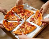 Ręce sięgają po kawałki pysznego ciasta na pizzę z kiełbasą i grzybami.