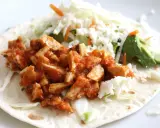 Pyszna tortilla z kurczakiem w sosie, posypana serem feta, z dodatkiem świeżej sałaty i awokado.