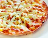 Pyszna pizza z tortilli, obficie posypana serem i ziołami, pokrojona na trójkątne kawałki.