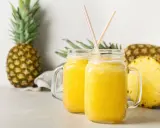 Orzeźwiający drink w ananasie, podany w słoikach, z kawałkami ananasa w tle.