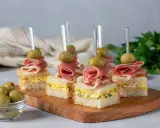 Eleganckie mini przekąski na imprezę: kanapki z szynką, jajkiem i oliwkami na drewnianej desce.