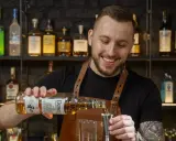 Uśmiechnięty barman, który robi drinki, nalewa whisky Dewar's do jiggera.