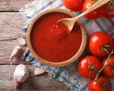 Domowy sos do pizzy z koncentratu, czosnek i świeże pomidory na drewnianym blacie.