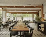Elegancka sala restauracyjna z długimi stołami, idealna na degustację **primitivo kuchnia i wino**. Drewniane belki i duże okna tworzą przytulną atmosferę.