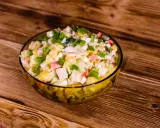 Pyszna sałatka z surimi, z kukurydzą, jajkiem i szczypiorkiem, podana w szklanej misce na drewnianym blacie.