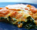 Pyszne lasagne ze szpinakiem, z pomarańczowym sosem i ciągnącym się serem, na granatowym talerzu.