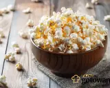 Pyszny popcorn w drewnianej misce, rozsypany na stole. Czy da się zrobić popcorn w piekarniku? Tak, i wygląda równie apetycznie!