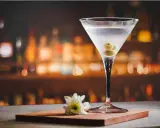 Eleganckie drinki z martini, ozdobione oliwkami, stoją na blacie baru. Obok kieliszka leży biały kwiat.