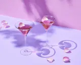 Dwa różowe drinki w kieliszkach do martini, ozdobione płatkami róż. Idealne co do martini na romantyczny wieczór.