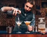 Barman przygotowuje drinki, zastanawiając się, jaki rum do mojito będzie najlepszy. Na blacie stoją kieliszki i karafka z bursztynowym płynem.