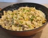 Tagliatelle z kurczakiem w sosie śmietanowym, posypane szczypiorkiem, podane w patelni. Pyszne danie gotowe do spożycia.