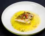 Filet ryby w aromatycznym sosie cytrynowym, podany na plastrach ziemniaków.