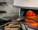 Piec do pizzy z rozżarzonymi węglami. Łopatka czeka, by włożyć do środka pizzę, która będzie piec się w 200 stopniach.