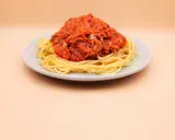 Porcja spaghetti z sosem pomidorowym i tuńczykiem, podana na jasnym talerzu.