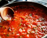 Gęsty, aromatyczny sos do spaghetti gotuje się na patelni. Drewniana łyżka miesza pomidorową masę z ziołami.