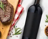 Idealne jakie wino do steka? Soczyste steki na desce, butelka czerwonego wina i przyprawy.