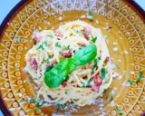 Pyszne spaghetti carbonara ze śmietaną, posypane parmezanem i natką pietruszki, ozdobione listkiem bazylii.