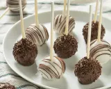 Pyszne cake pops przepis na talerzu: czekoladowe z posypką i białe z polewą.