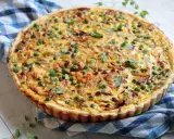 Pyszna tarta z porem i boczkiem, udekorowana groszkiem i ziołami, na niebiesko-białej kratce.