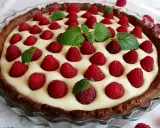 Pyszna tarta z białą czekoladą i malinami, ozdobiona listkami mięty. Idealna na deser.