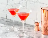Dwa kieliszki z czerwonym drinkiem, idealne na letnie wieczory. W tle miedziany shaker i miarka, sugerujące przygotowanie drinka bacardi ze spritem.