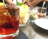 Czerwony drink z lodem i cytryną, obok chipsy i oliwki. Idealny na aperitif, jak zrobic martini?