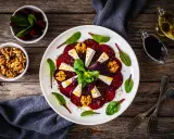 Eleganckie carpaccio z buraka z serem feta, orzechami włoskimi i świeżymi ziołami, podane na białym talerzu.