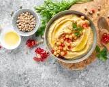 Pyszny hummus z ciecierzycy, udekorowany pestkami granatu i natką pietruszki, obok cytryny i oliwy.