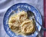 Pyszny makaron alfredo przepis na talerzu z widelcem i łyżką, posypany startym parmezanem.