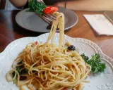 Widok z bliska na talerz pysznego spaghetti aglio e olio, z widelcem unoszącym porcję makaronu, pomidorkiem i bazylią.
