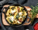 Pyszne fusilli ze szpinakiem i suszonymi pomidorami, posypane parmezanem i kawałkami sera feta.