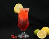 Orzeźwiający drink z granatem, ozdobiony plasterkiem cytryny. Obok leżą świeże owoce: cytryna i limonka.