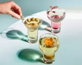 Eleganckie drinki z wódką: martini z oliwkami, różowy koktajl i złoty napój z kwiatem.