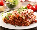 Pyszne cannelloni z mięsem mielonym, polane sosem pomidorowym i posypane parmezanem, na talerzu z pomidorami i sałatką.