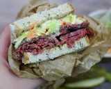 Pyszna kanapka z pastrami, z chrupiącą surówką i musztardą, zawinięta w papier.