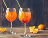 Dwa orzeźwiające drinki z aperolem i sokiem pomarańczowym, ozdobione plasterkami pomarańczy i podane z kolorowymi słomkami. Idealne na letnie popołudnie.